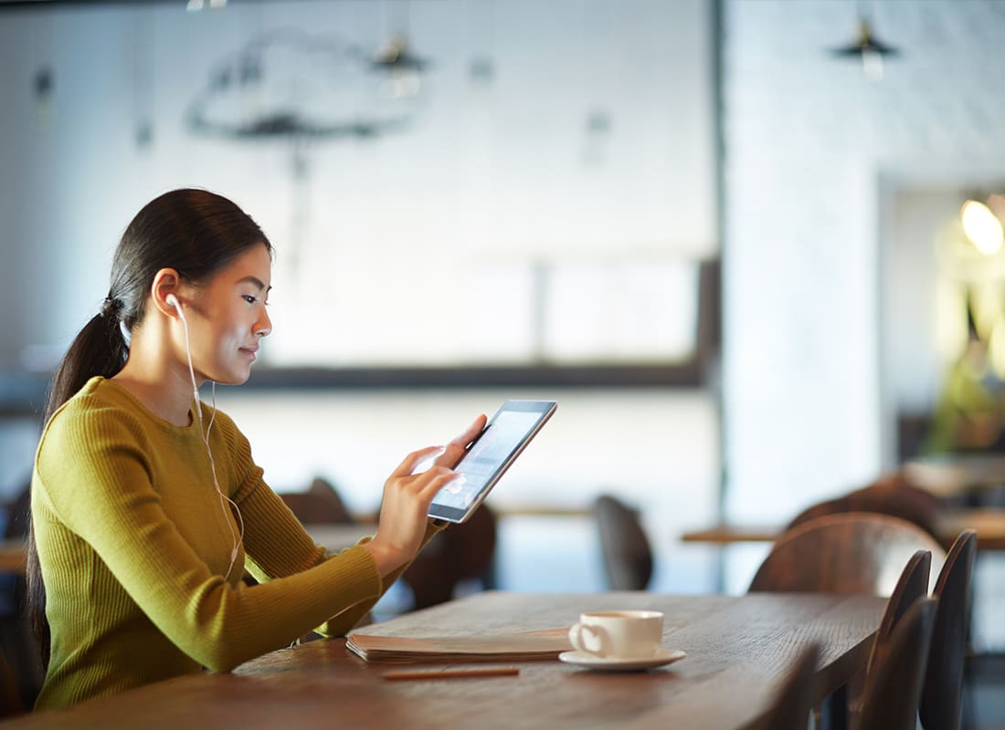 Video Library - Woman Sitting at Long Table in a Cafe While Watching a Video on Her Tablet with Headphones in